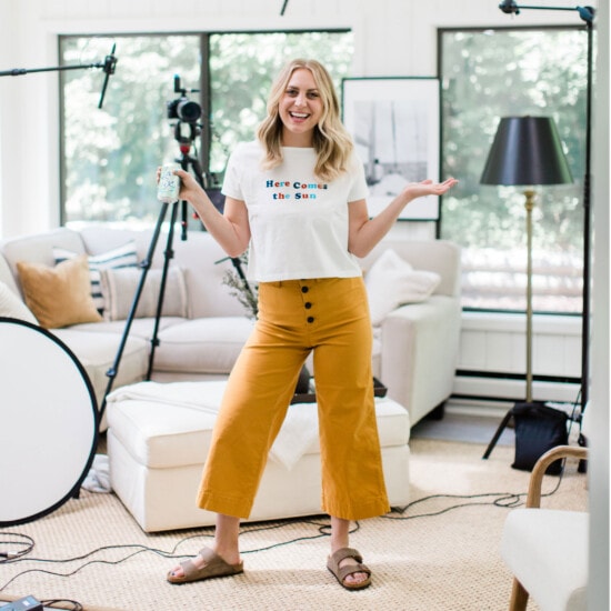 A blonde foodie stands in front of a camera in a living room.