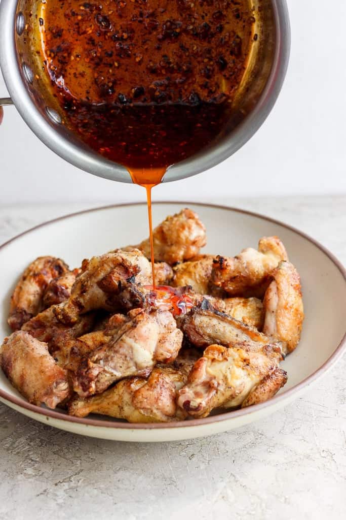 Pouring sauce over a plate of cooked chicken wings.