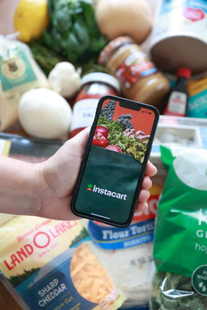 A person holding a phone next to a bunch of groceries.