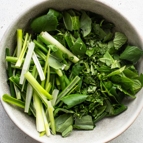 Fresh herbs in a bowl on a white surface.