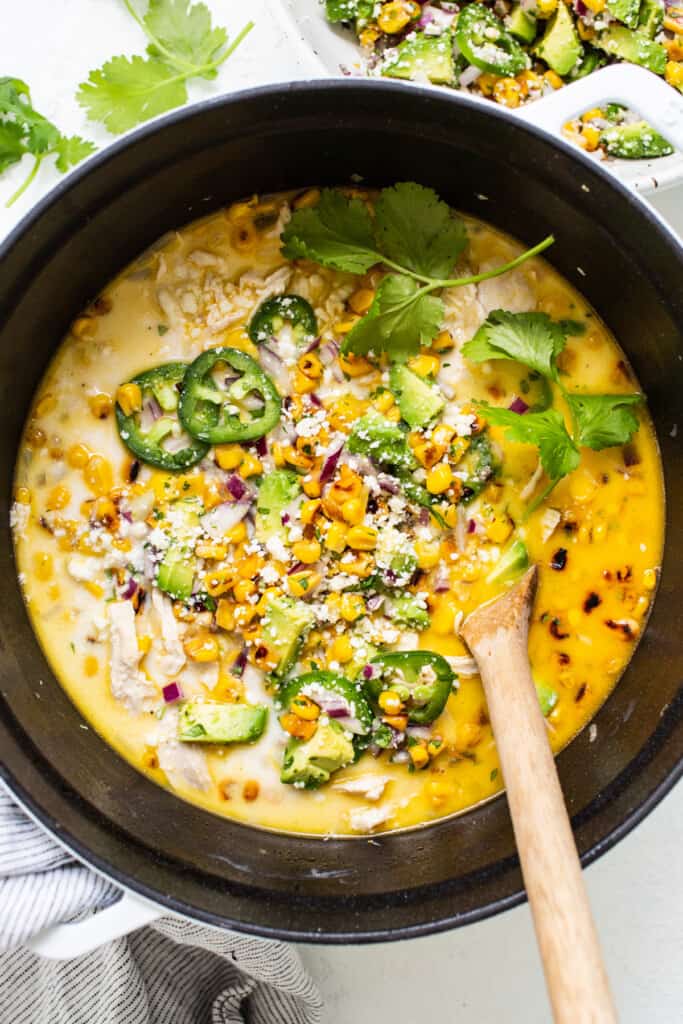 Chicken and corn soup in a pan with a wooden spoon.