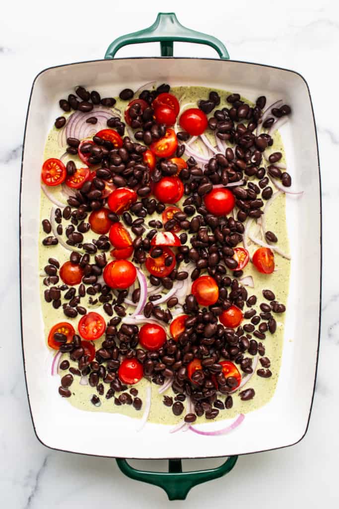 A baking dish with black beans, cherry tomatoes, and sliced onions, ready for cooking.