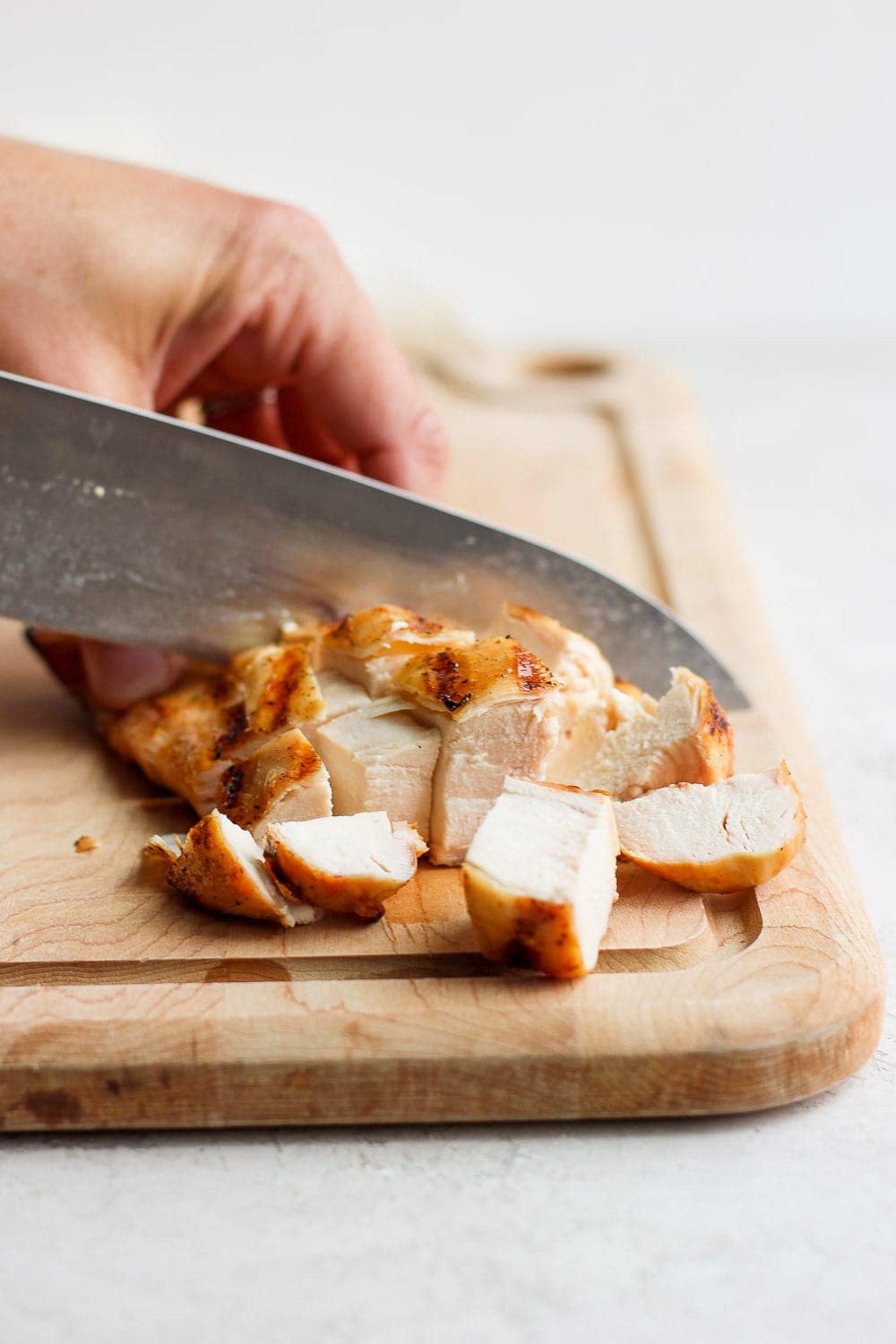 knife cutting chicken breast on cutting board.