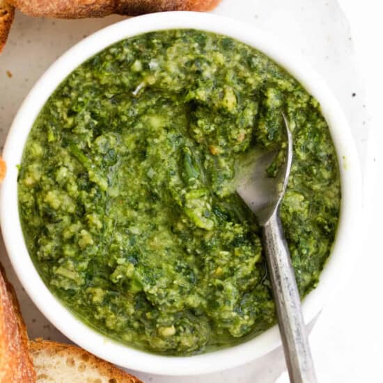 A bowl of homemade pesto with bread and a spoon.