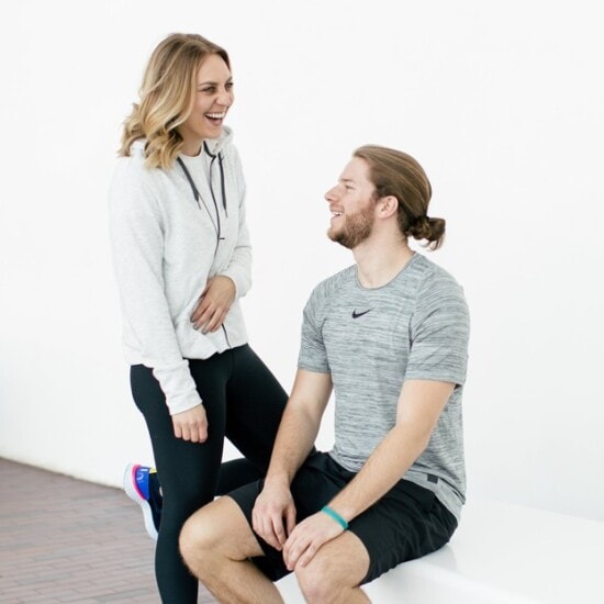 A man and woman sitting on a bench laughing while wearing Nike Epic React shoes.