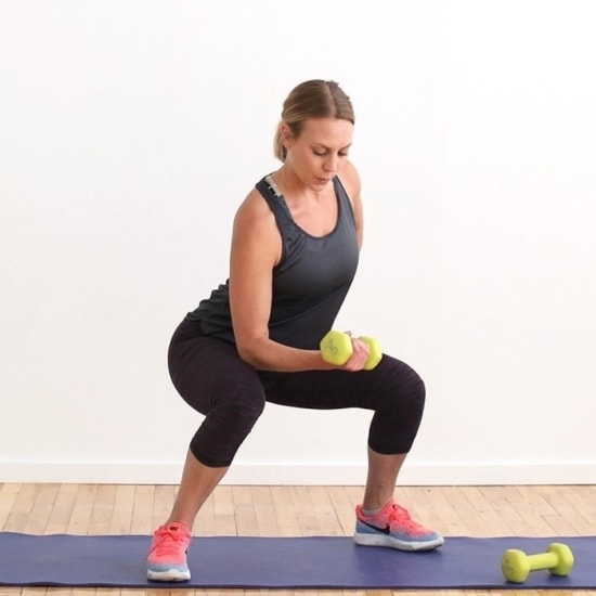 A woman incorporating dumbbells into her 2-3-2 workout routine by doing squats.