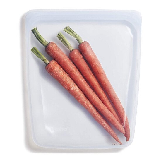 Three carrots are in a plastic bag on a white surface.